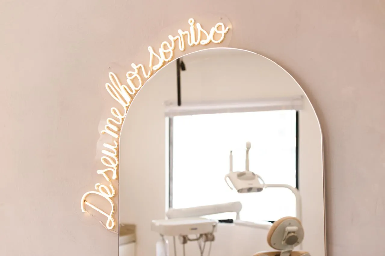 Neon com a frase Dê o seu melhor sorriso sobre o espelho em arco do consultório